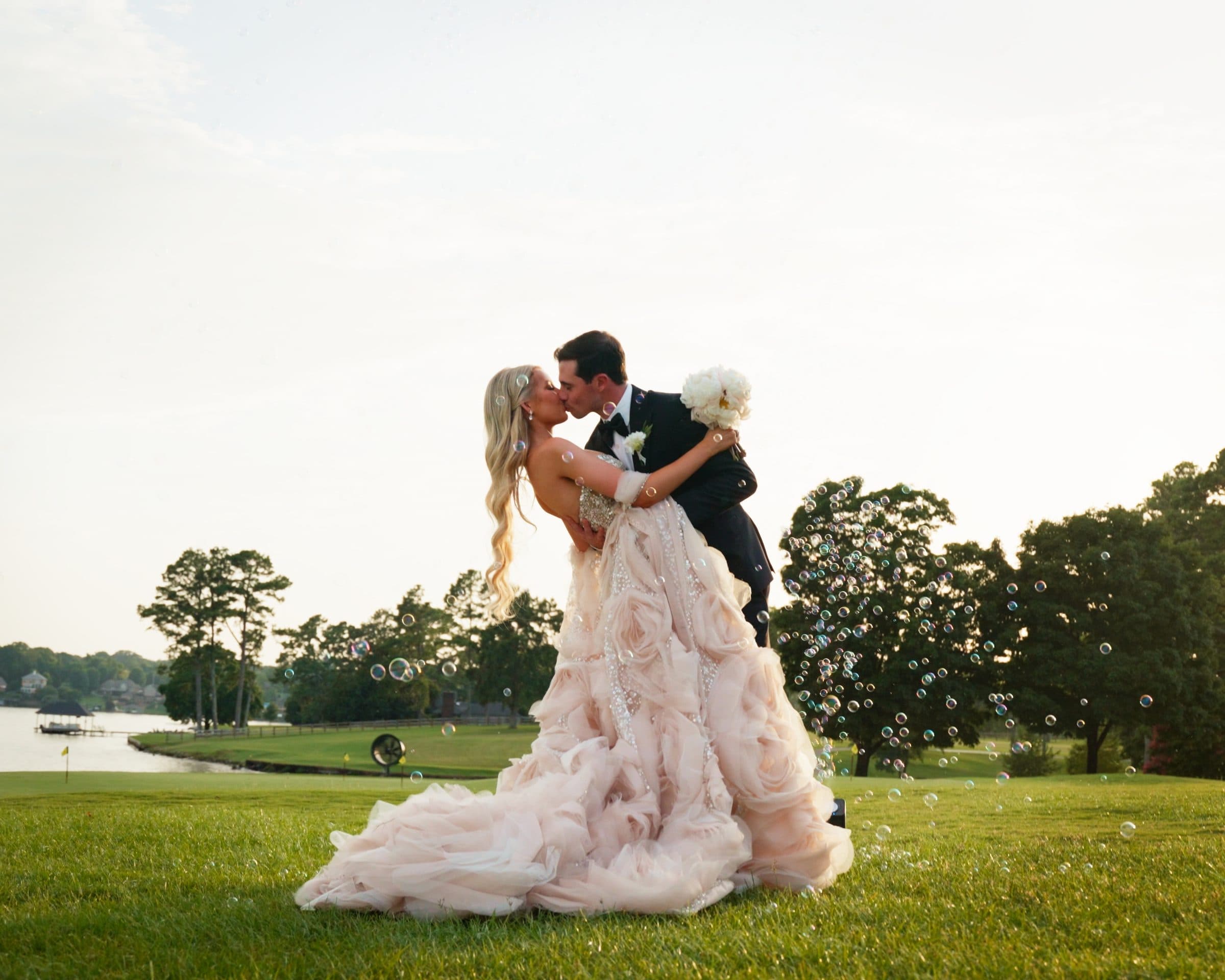 A couple kissing on the lawn by the lake, bubbles in the air, at golden hour