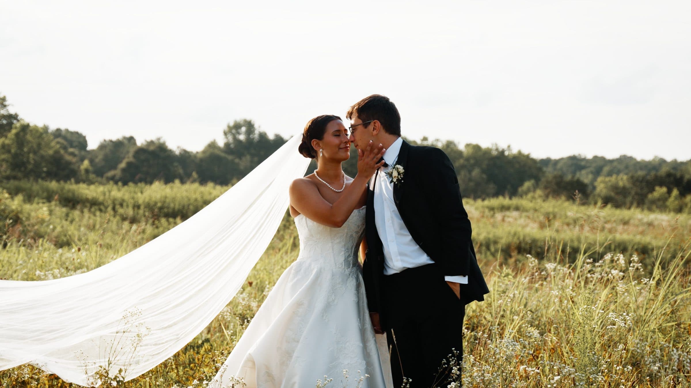 A couple in a field at golden hour, the veil caught in the wind