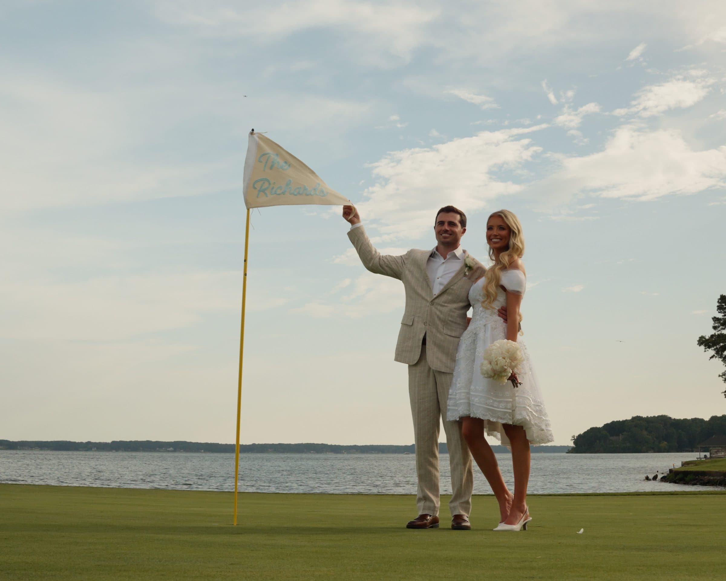 A couple on a lakeside golf green holding a flag with their new name on it